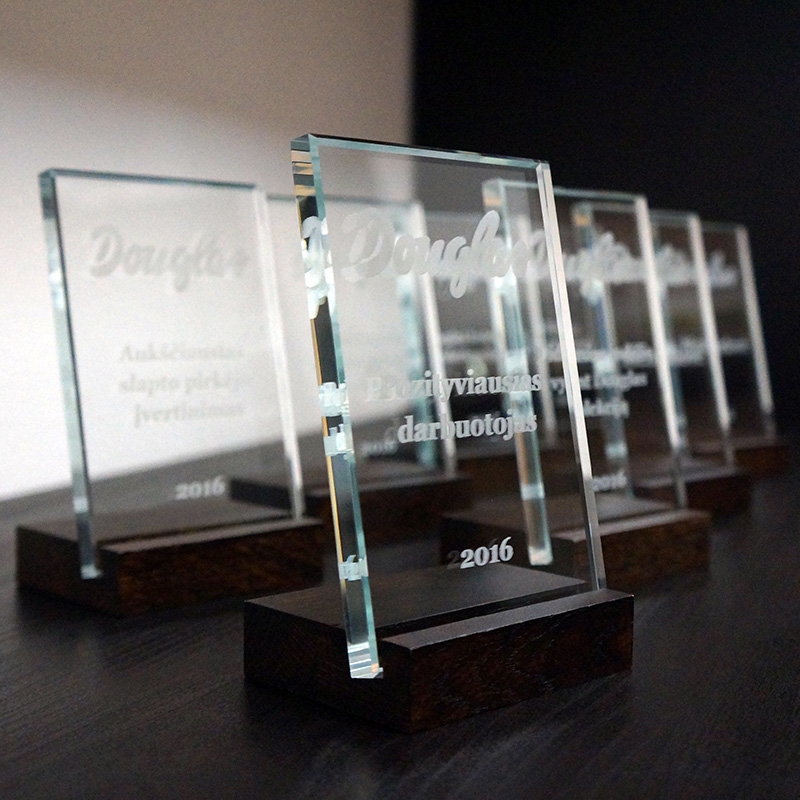 Stikliniai apdovanojimai su užrašu Douglas darbuotojams, padėka už metų nuopelnus, ant medinio pagrindo.